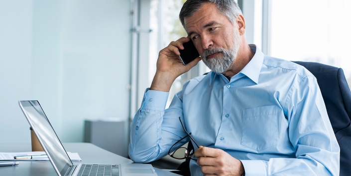Executive senior businessman using his mobile phone and talking wih somebody while working laptop in the office.